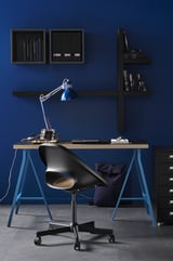 Moderner Arbeitsplatz mit blauem Thema mit schwarzem ELDBERGET-Stuhl, blauer Lampe und dunklen Regalen für Bücher und Akten.