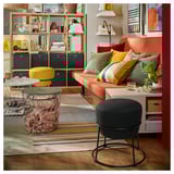 Stilvolles Wohnzimmer mit EMMISLÖV-Hockern in Gelb und Schwarz, modernem Design, buntem Sofa und Holzregalen.
