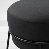 Runder gepolsterter Hocker mit dunkelgrauem Stoff über Metallgestell, der robust und modern wirkt.