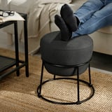 Eine Person entspannt sich auf einem Sofa mit den Füßen auf einem EMMISLÖV-Hocker, der seine Verwendung als Fußstütze zur Schau stellt.