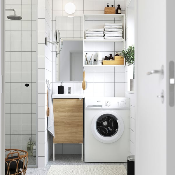 Moderne kompakte Wäscherei. Weiße Waschmaschine, schlanke Regale, verspiegelte Tür. Ordentlich und effizient.