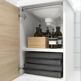 Offener Badezimmerschrank mit zwei Regalen. Im oberen Regal befinden sich Toilettenartikel, im unteren befinden sich gerollte Handtücher.