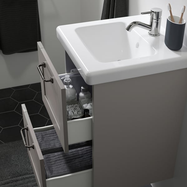 Moderner Badezimmerwaschtisch mit offener Schublade mit Pflegeprodukten, darunter ein weißes Waschbecken und ein verchromter Wasserhahn.