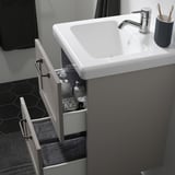 Moderner Badezimmerwaschtisch mit offener Schublade mit Pflegeprodukten, darunter ein weißes Waschbecken und ein verchromter Wasserhahn.