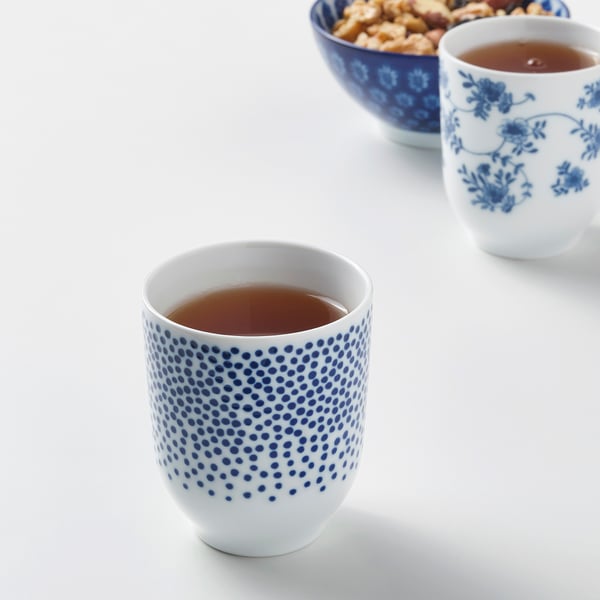 Zwei blau-weiß gemusterte Tassen mit Tee, eine geblümt, eine gepunktet, neben einer Schüssel mit Snacks.