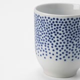 Porzellantasse mit weißem und blauem Punktmuster, glattem Rand und glänzender Oberfläche. Elegantes und detailliertes Design.