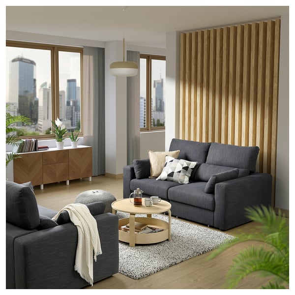 Modernes Wohnzimmer mit grauem ESKILSTUNA-Sofa, Wollteppich, Couchtisch aus Holz und Stadtblick.