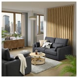 Modernes Wohnzimmer mit grauem ESKILSTUNA-Sofa, Wollteppich, Couchtisch aus Holz und Stadtblick.