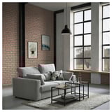 Modernes Wohnzimmer mit grauem ESKILSTUNA-Sofa, Backsteinwand, großen Fenstern und hängender Pendelleuchte.