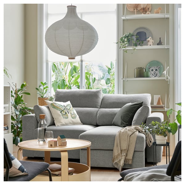 Modernes Wohnzimmer mit grauem ESKILSTUNA-Sofa, hölzernem Couchtisch, großem Fenster und Hängelampe.