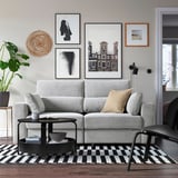 Modernes Wohnzimmer mit grauem Sofa, schwarzem Tisch, Pflanzen und Kunstwerken.
