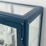 Glastürschrank mit Metallrahmen und Regalen für Sammlerstücke oder Spiele.