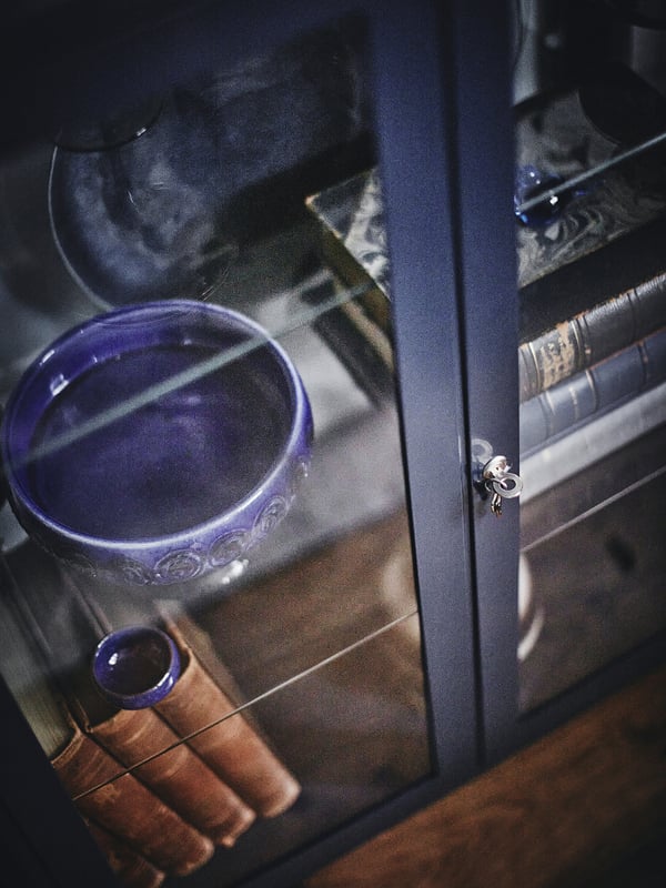 Glastürschrank FABRIKÖR mit blauer Schale, Schlüsseln und Büchern, mit verstellbaren Einlegeböden und Türschloss mit Metallschlüsseln.