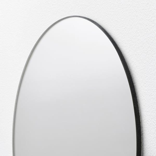 Ovaler Spiegel mit schlankem Rand, an der Wand montiert, reflektiert das Licht sanft.