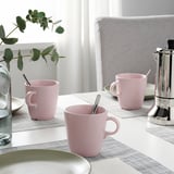 Drei rosa Tassen und eine Kaffeemaschine auf dem Tisch mit Tischsets; Dekorative Pflanzen.