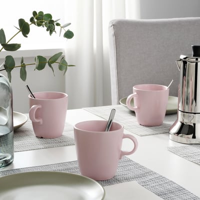 Drei rosa Tassen und eine Kaffeemaschine auf dem Tisch mit Tischsets; Dekorative Pflanzen.