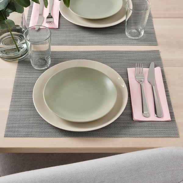 Tischdekoration mit zwei Tischsets, Tellern, Gläsern, Besteck und Servietten.