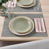 Tischdekoration mit zwei Tischsets, Tellern, Gläsern, Besteck und Servietten.