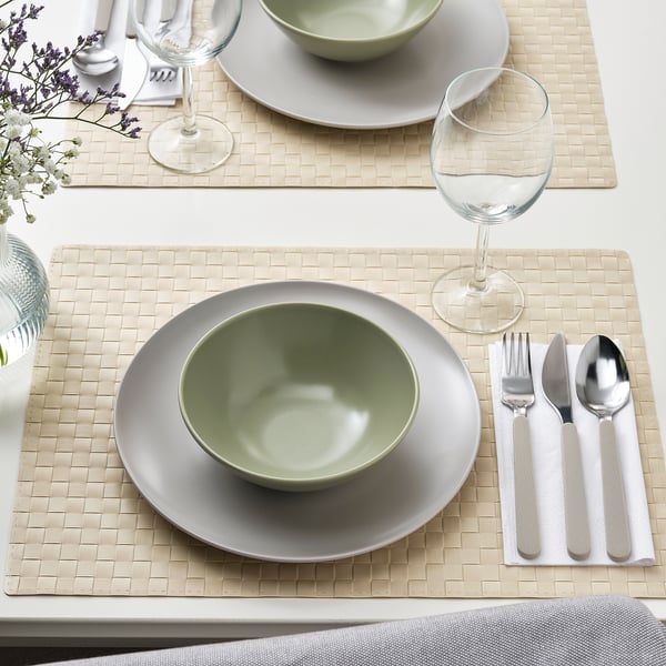 Gedeckter Tisch mit FÄRGKLAR Tellern, Schalen und Gläsern auf geflochtenen Matten, bereit zum Essen.