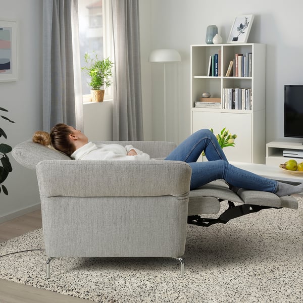 Eine Frau lehnt sich mit hochgelegten Füßen auf einem FAMMARP-Stuhl in einem Wohnzimmer zurück und genießt dessen Bequemlichkeit. Neben ihr ein Bücherregal und ein Fernseher.