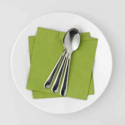 Ein Teller mit grünen Papierservietten und drei Metalllöffeln. Servietten sind saugfähig und dekorativ für den gedeckten Tisch.