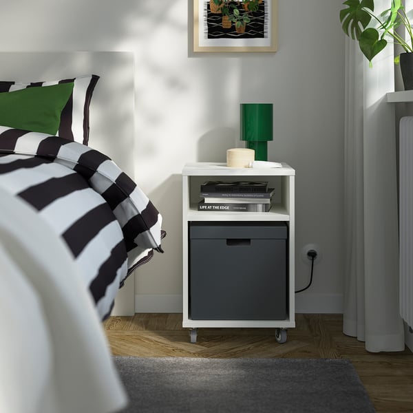 Kleine weiß-graue FJÄDERHARV-Box neben dem Bett, mit Büchern und Kerze.