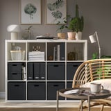 Modernes Wohnzimmer mit Kallax-Regal, Korbstuhl und Wandkunst.