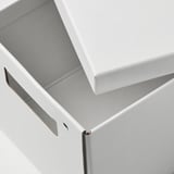Geschlossener weißer Karton, sauber gefertigt mit sichtbarem Metallverschluss, auf einer ebenen Fläche sitzend.