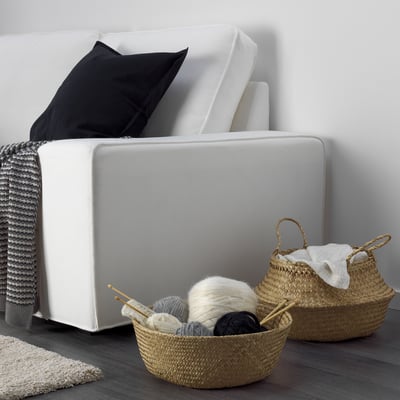 Ein weißes Sofa mit geflochtenen Körben darunter, in denen Garn und Stricknadeln liegen.