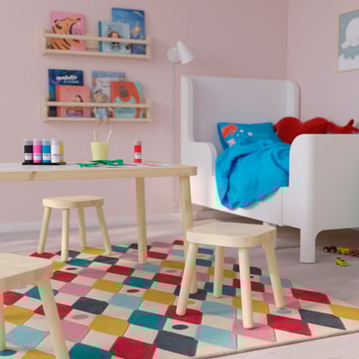 Kinderzimmer mit FLISAT Tisch & Hockern. Helles Holz, kleine Größe, bunter Teppich. Bücher & Spielzeug in der Nähe.