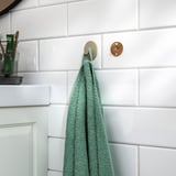 Ein grünes Handtuch hängt an einer Wandschiene mit einem abnehmbaren Tablett, ideal für die Aufbewahrung und Organisation im Badezimmer.