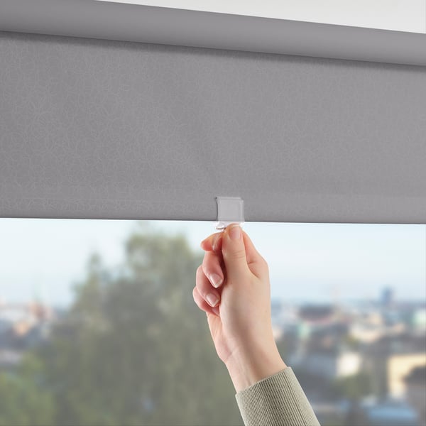 Handhebendes graues Rollo mit kreisförmigem Muster, blockierendes Licht, im Fenster montiert.