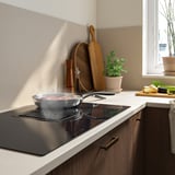 Moderne Küche mit einem eleganten, schwarzen Induktionskochfeld mit integrierter Dunstabzugshaube und einer Pfanne.