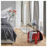 Rote Ottomane im gemütlichen Schlafzimmer mit grauem Bett, Beistelltisch mit Blumen.