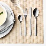 Ordentlich gedeckter Tisch mit FÖRNUFT Edelstahlbesteck: Gabel, Messer, Löffel und eine Schüssel Suppe auf einem beigen Tischset.