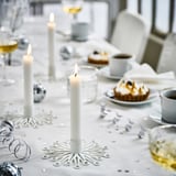 Eleganter weißer FRÖJDA-Kerzenständer in der Mitte, winzige Flammen, zierliches Dekor inmitten von Leckereien, Gläsern und Besteck. Klein, aber auffällig.