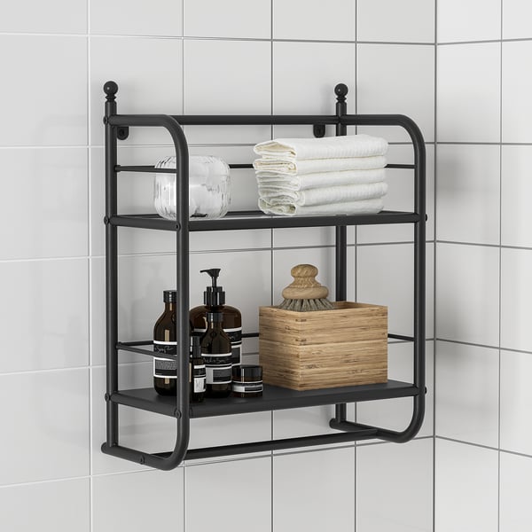 Schwarzes Badezimmerregal aus Metall mit Handtüchern, Flaschen und einer Holzkiste an einer gefliesten Wand.
