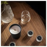 Stellen Sie sich einen Holztisch mit zwei Glasbechern und drei Kerzen vor: eine große schwarze Kerze und zwei kleinere silberne.