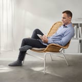 Stuhl aus natürlichem Korbgeflecht mit sitzendem Mann, der Papier hält. Schlankes Design für Komfort.
