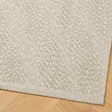 Hochwertiger, beigefarbener Webteppich auf Holzboden, der eine komplizierte Textur und Handwerkskunst zeigt.