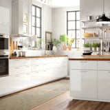 Moderne weiße Küche mit Holztheken, großen Fenstern, eleganten Geräten und Teppich.