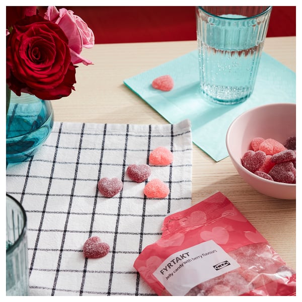 Ikeas FYRTAKT Gelee-Bonbontüte mit herzförmigen Süßigkeiten, von denen einige herausquellen, neben einer Schüssel und Rosen.