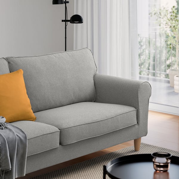 Modernes Wohnzimmer mit hellgrauem GÄLLTOFTA-Zweisitzer , schwarzer Lampe und kleinem Tisch.
