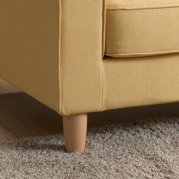 Modernes Sofa aus senfgelbem Stoff mit klaren Linien und Holzbeinen auf flauschigem weißem Teppich.