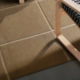 Brauner handgewebter Wollteppich auf dem Boden, mit Holzstuhl auf der rechten Seite.