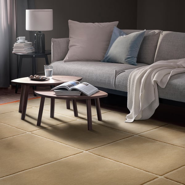 Modernes Wohnzimmer mit grauem Sofa, lila und blauen Kissen, Couchtischen aus Holz, Lampe, Büchern und GÅSHIRS-Teppich.