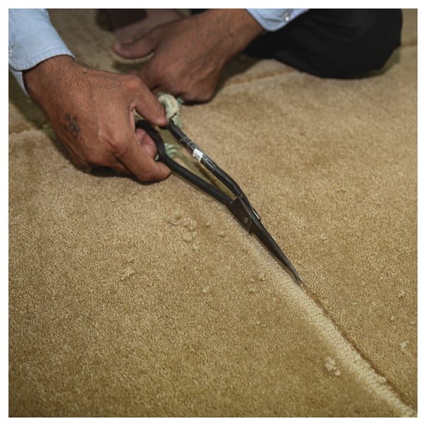 Person schneidet beige GÅSHIRS Wollteppich mit einer Schere zu. Handgefertigt, natürlich, langlebig.