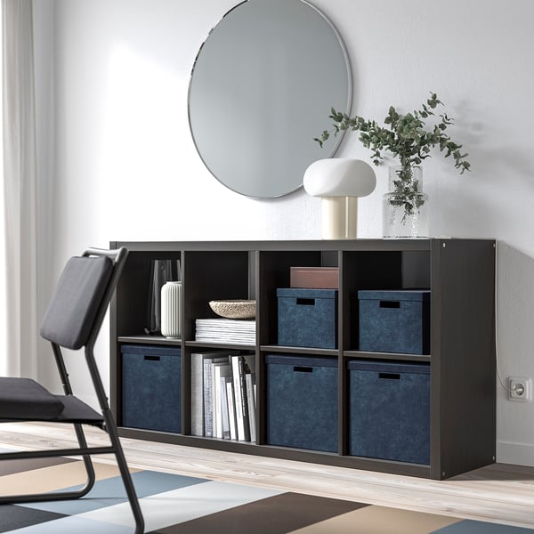 Moderner Wohnraum mit GJÄTTA Aufbewahrungsboxen aus Samt in Blau auf dunklem Regal, gepaart mit einem runden Spiegel und einem grauen Stuhl.