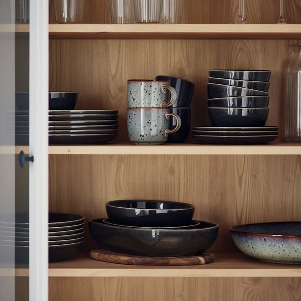 GLADELIG, graues Geschirr, Steinzeug, auf Regalen gestapelt. Größere Teller, Tassen, Schalen, einzigartiges Design.