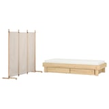 Dieses Bild hat das IKEA GLAMBERGET Set: ein helles, klappbares Bett aus Holz und einen beigen Raumteiler.